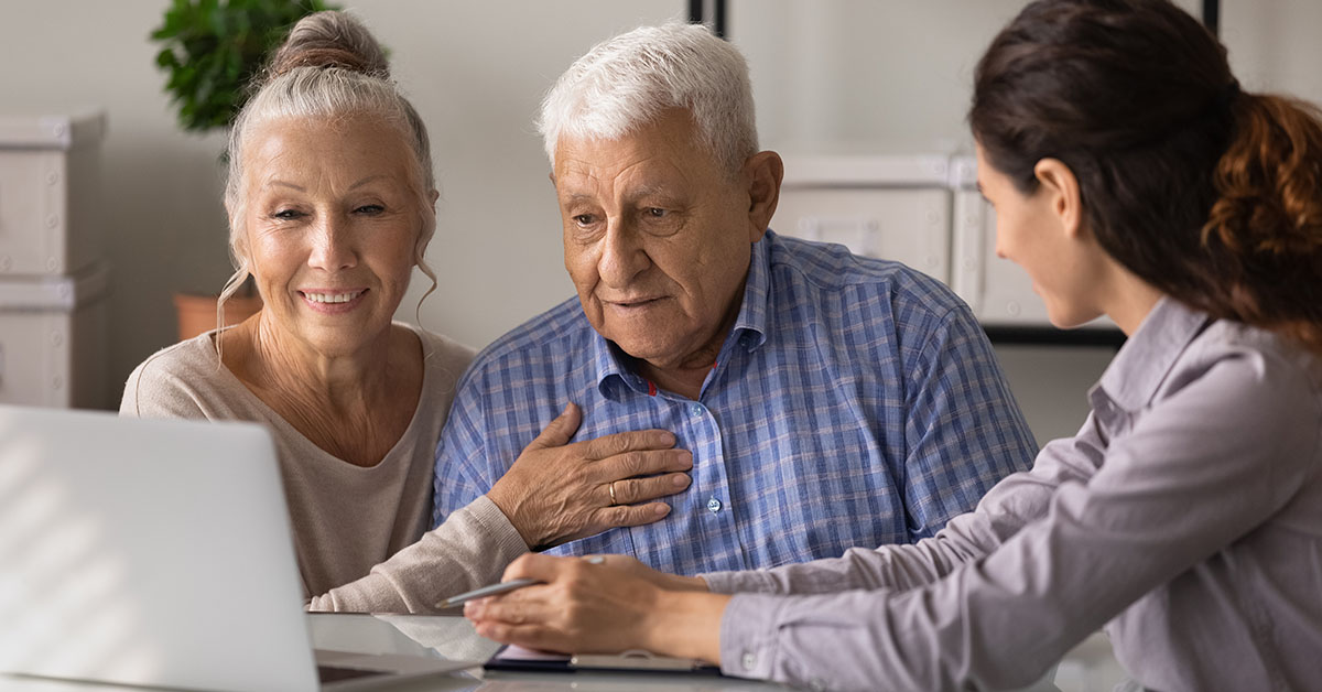 A retired couple sits with a financial advisor, reviewing information on a laptop together in a bright, modern office.