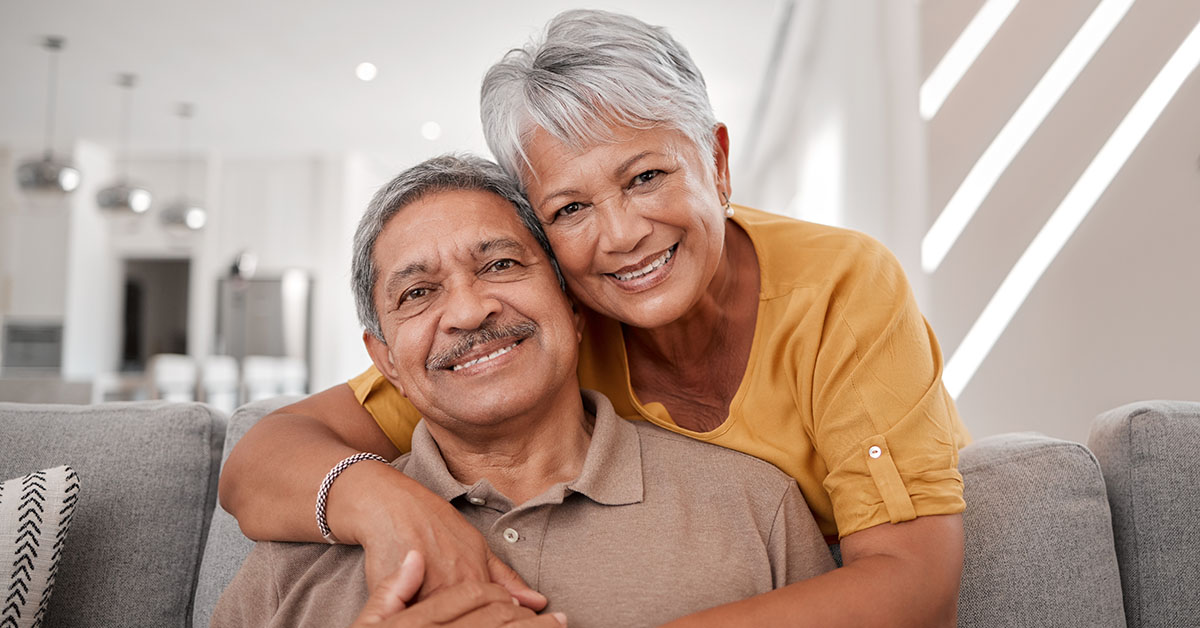 A smiling older couple sitting on a couch, embracing warmly, symbolizing gratitude, financial stability, and resilience—key themes in the "Five Things Investors Can Be Thankful For" article.