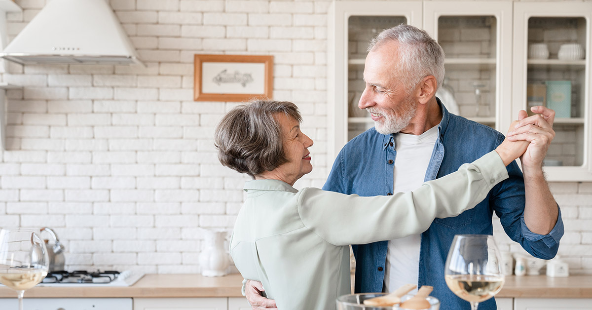 An older couple dancing together in their kitchen, reflecting joy, serenity, and the confidence that comes from long-term financial planning.