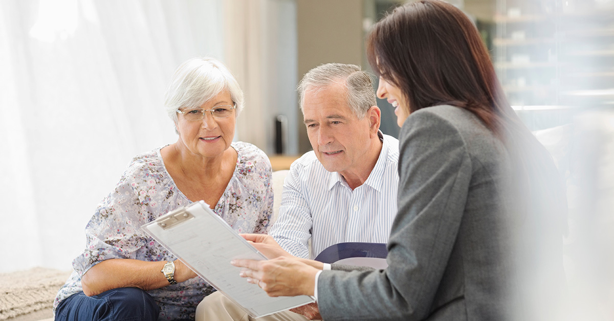 A Financial Gravity Family Office Director meeting with a retired couple in a bright modern office, calmly reviewing a long-term investment and tax plan together.