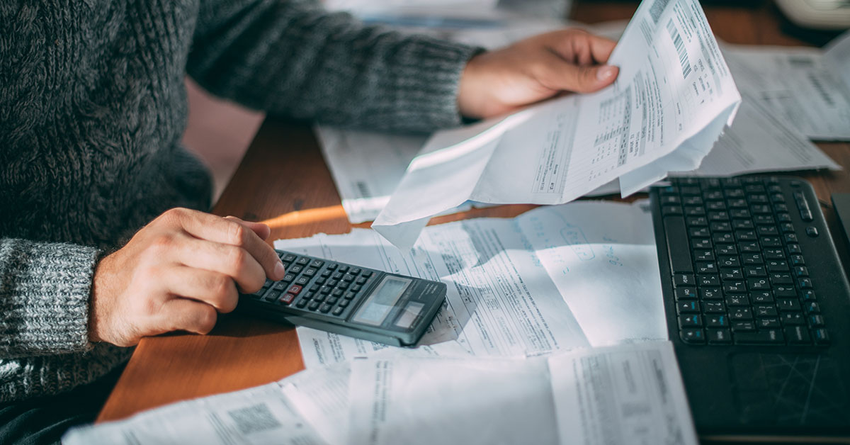 A person using a calculator and reviewing financial documents, illustrating the real-world impact of tariffs on household budgets and retirement planning.