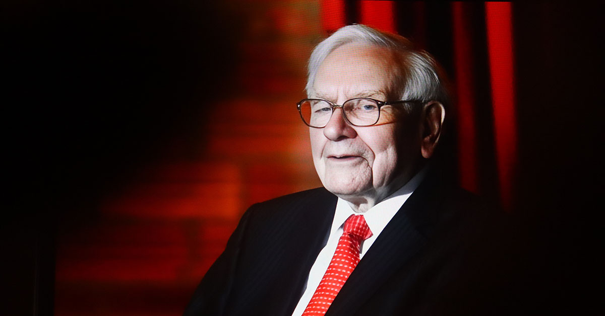 Warren Buffett in a dark suit and red tie, seated against a backdrop of warm red curtains, symbolizing enduring leadership and timeless wisdom.