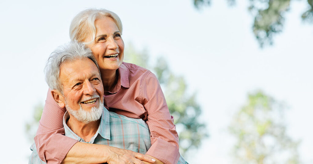 A happy senior couple outdoors, smiling and embracing, symbolizing financial security and enjoying retirement.