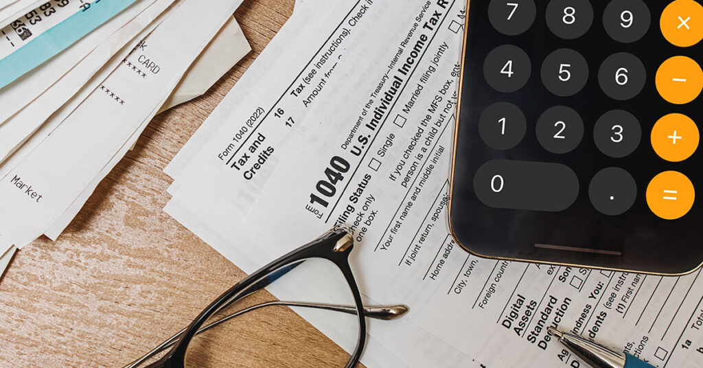 Tax documents, receipts, a smartphone calculator, and reading glasses on a wooden desk symbolize year-end tax planning and financial strategy.