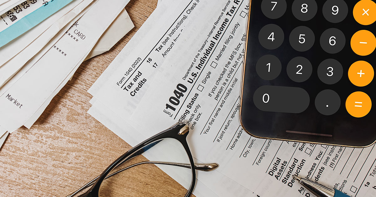 Tax documents, receipts, a smartphone calculator, and reading glasses on a wooden desk symbolize year-end tax planning and financial strategy.