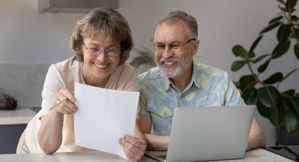 Smiling older couple reviewing financial documents at home, confident in their tax planning with Financial Gravity.