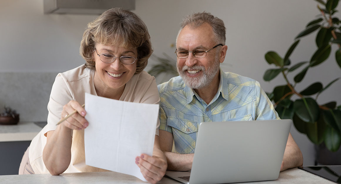 Smiling older couple reviewing financial documents at home, confident in their tax planning with Financial Gravity.