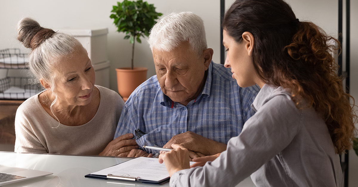 Older couple reviewing financial documents with a female advisor, symbolizing thoughtful risk management and long-term financial planning.